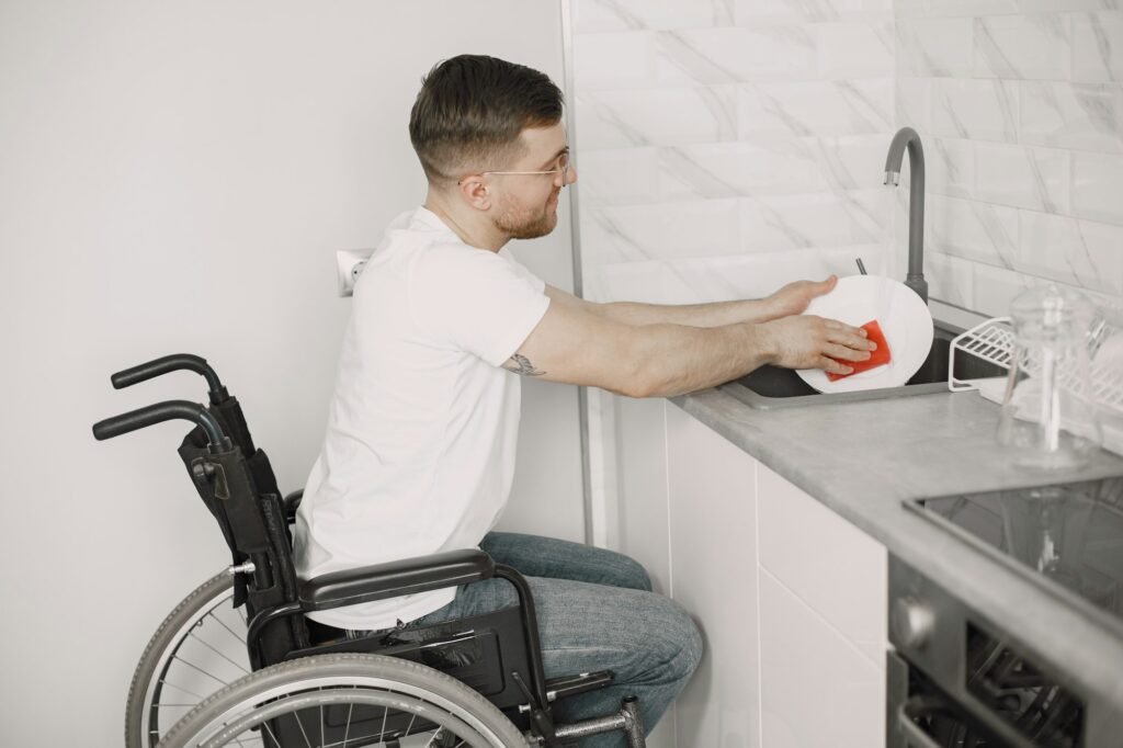 Young Happy Disabled Man On Wheelchair Washing Dishes